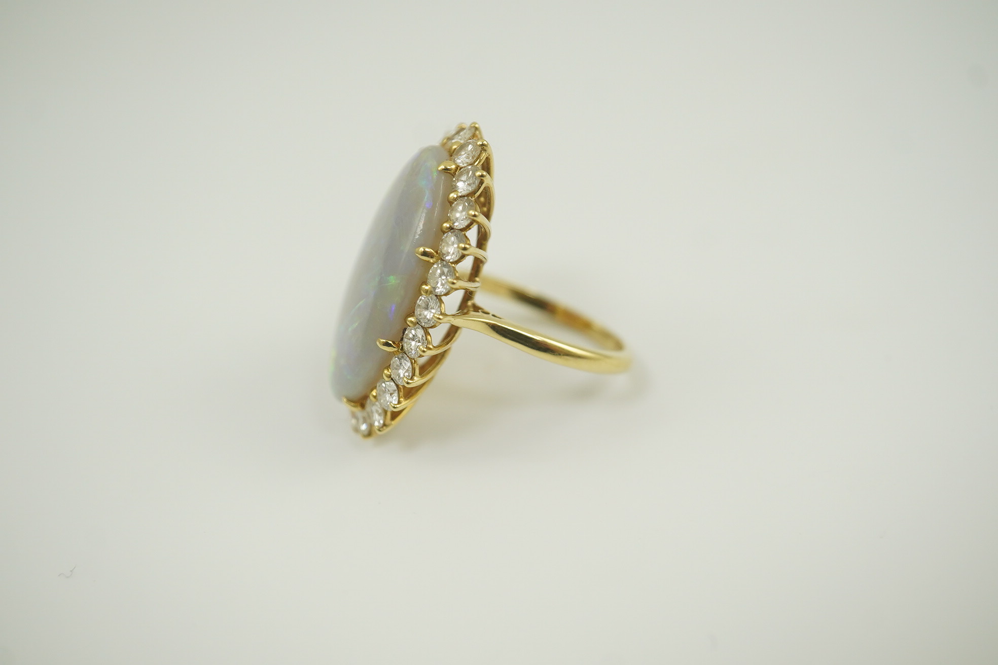 An 18ct gold, white opal and diamond set oval cluster dress ring, the cabochon opal measuring approximately 22mm by 14.5mm, with a depth of 5mm, and bordered by round brilliant cut diamonds, size L, gross weight 6.8 gram